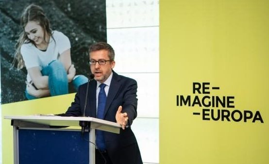 Photo of Carlos Moedas delivering a speech in an event with RIE logo in the background