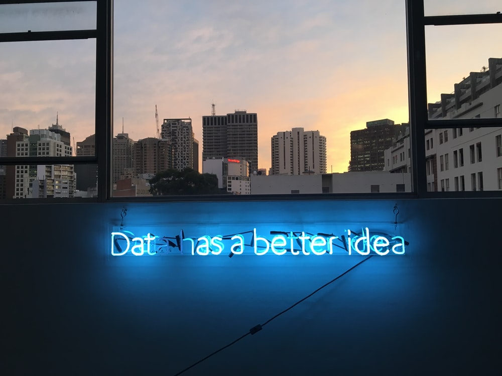 Blue Neon sign on a wall with a city and a sunset in the background