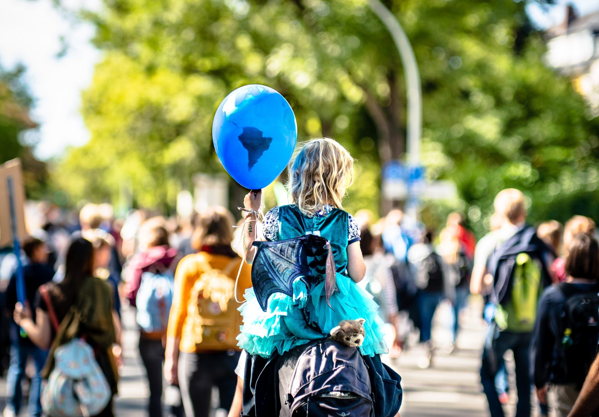 Child on the shoulders of an adult holding a ballon with planet earth with a protest in the background
