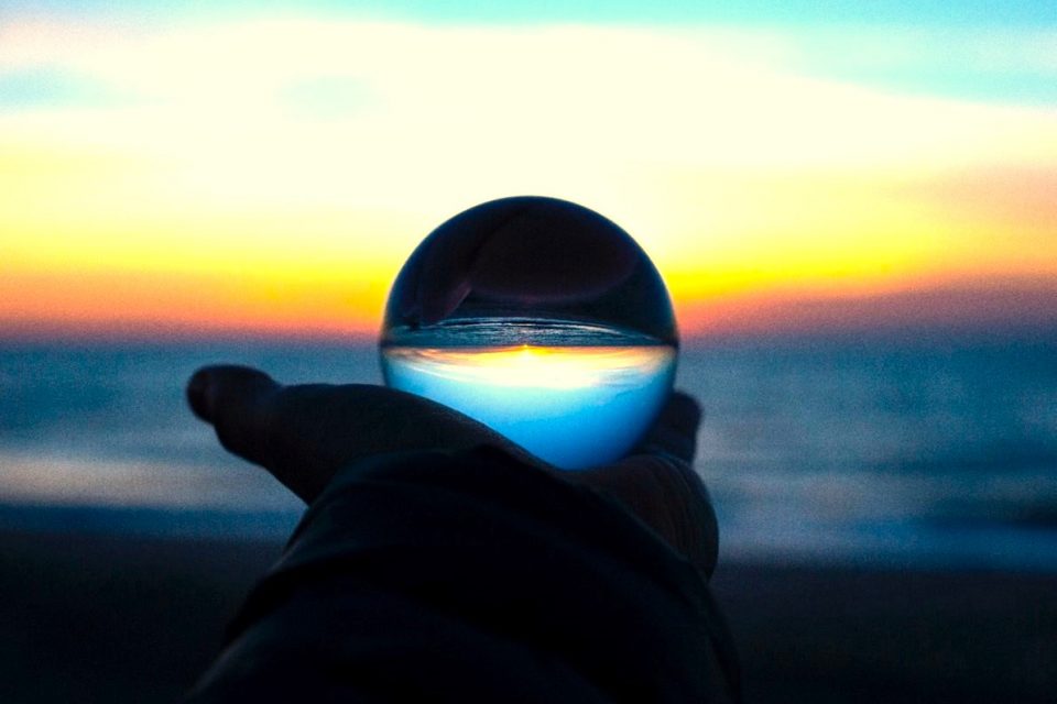shadow of a human hand holding crystal ball reflecting the sunset at the beach